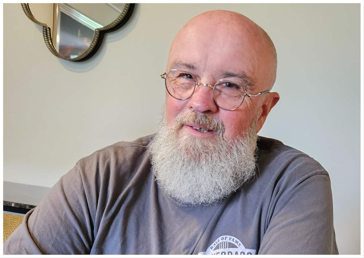 A man wearing glasses sits at a table, smiling. 