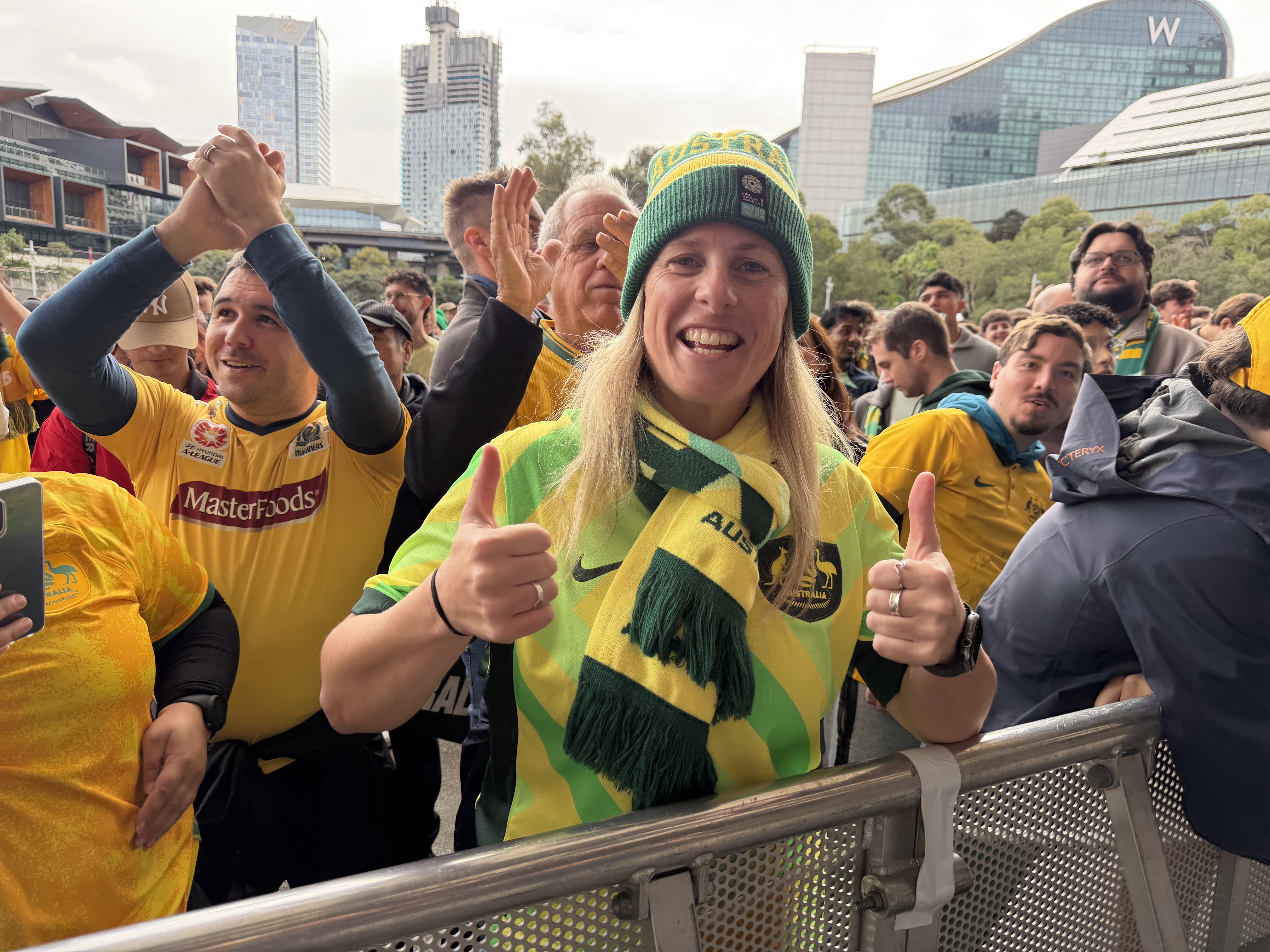 A woman wearing a Socceroos beanie posing with her thumbs up. 