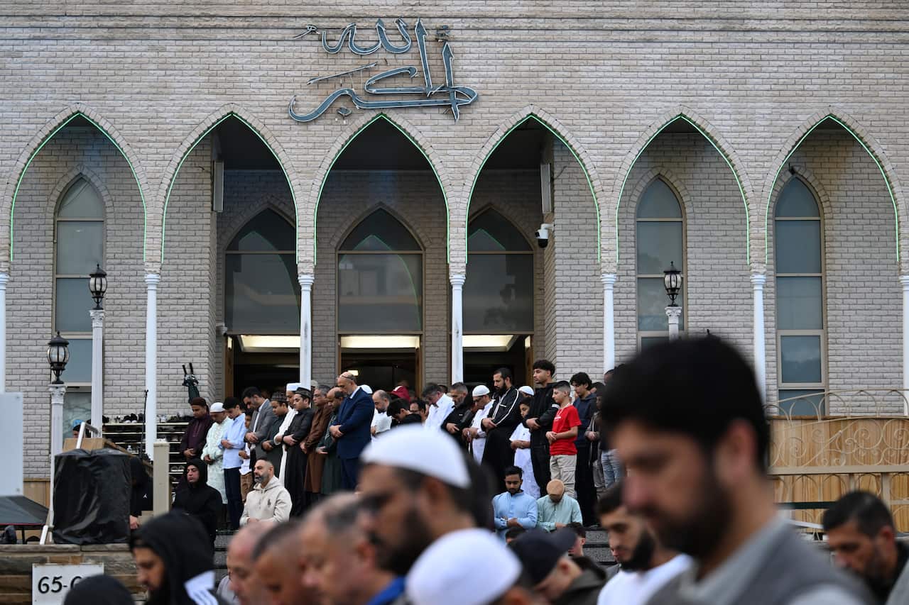Men stand with their heads bowed outside the mosque. 