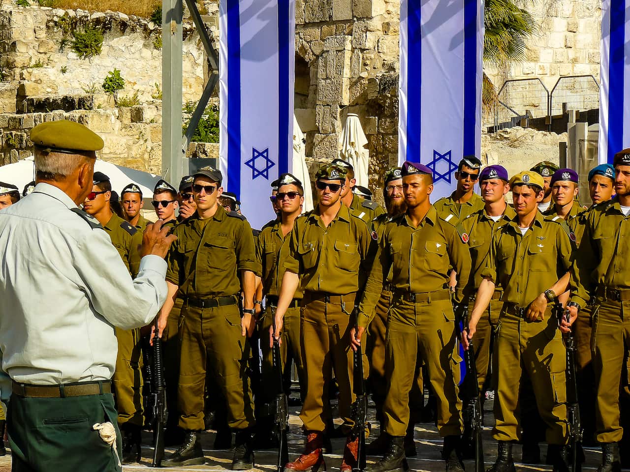 A group of IDF soldiers in uniform stand in front of the Israeli flag. 
