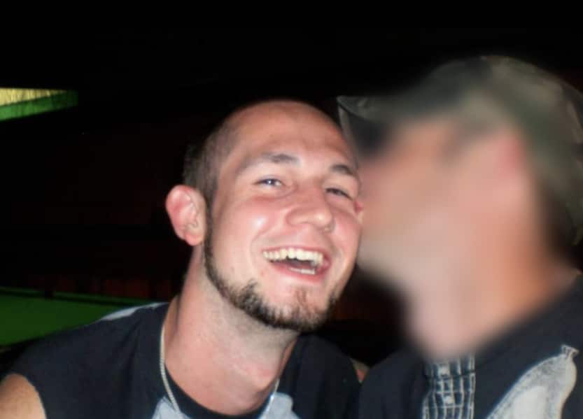 A man smiling as he's kissed by his male partner, whose face is blurred out.