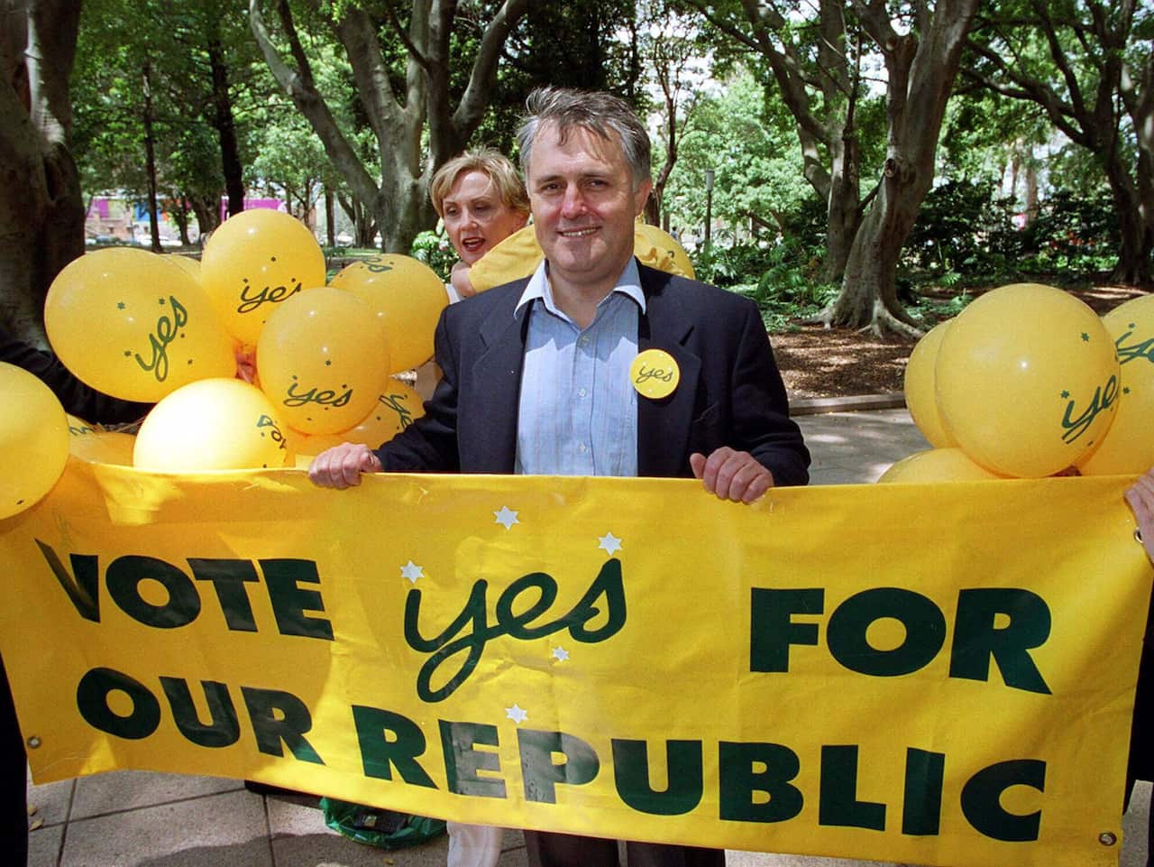 A man holding a yellow banner with green text that reads: Vote Yes for our republic