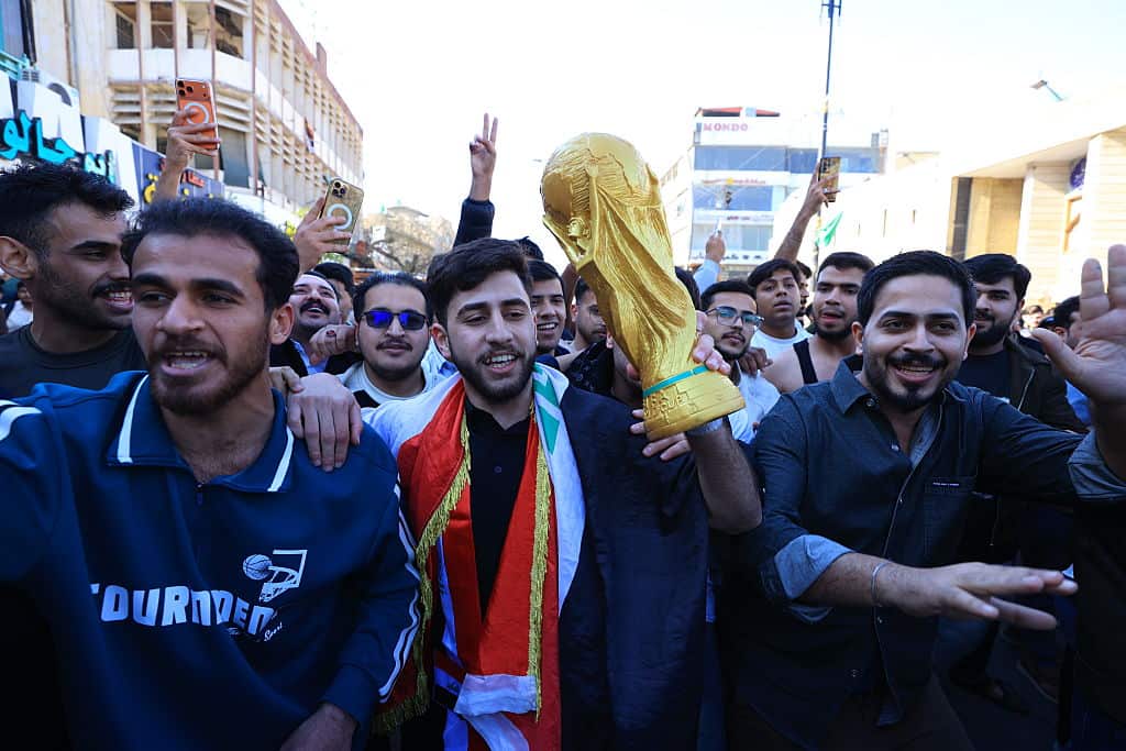 Crowds of people in a street. One is holding a replica gold trophy