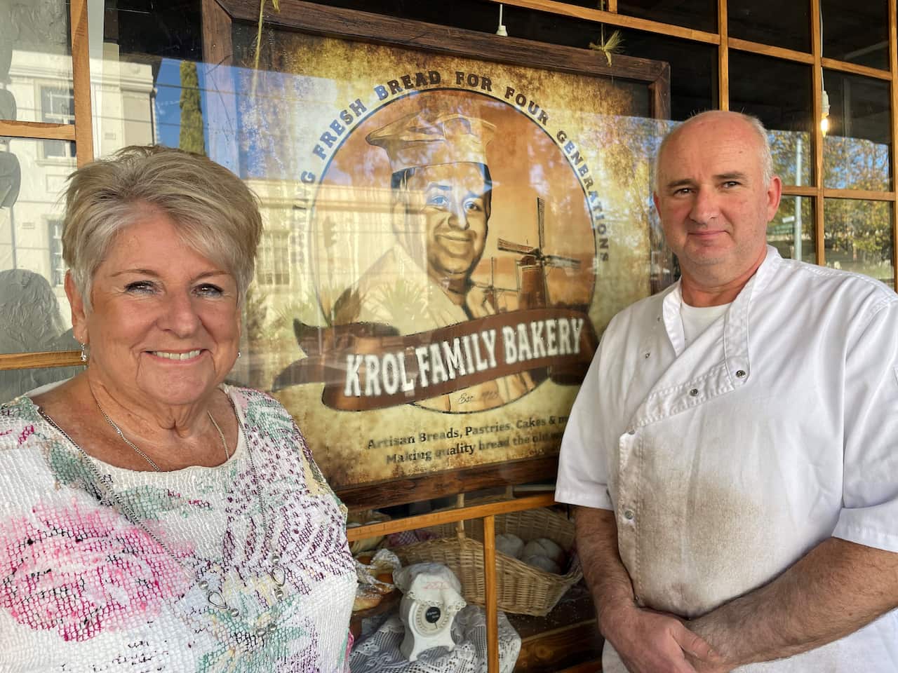 A woman in a floral shirt standing outside a shop with a man in a white jacket. 