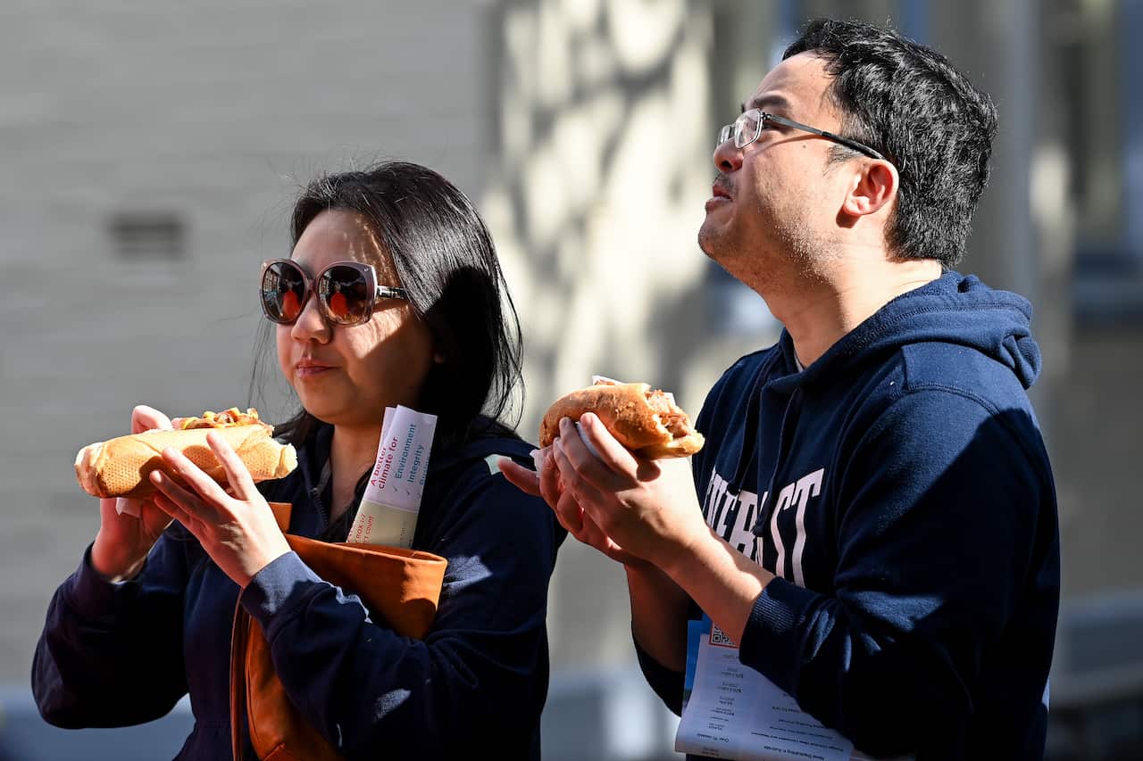Two people are seen holding sausages in a bread roll.
