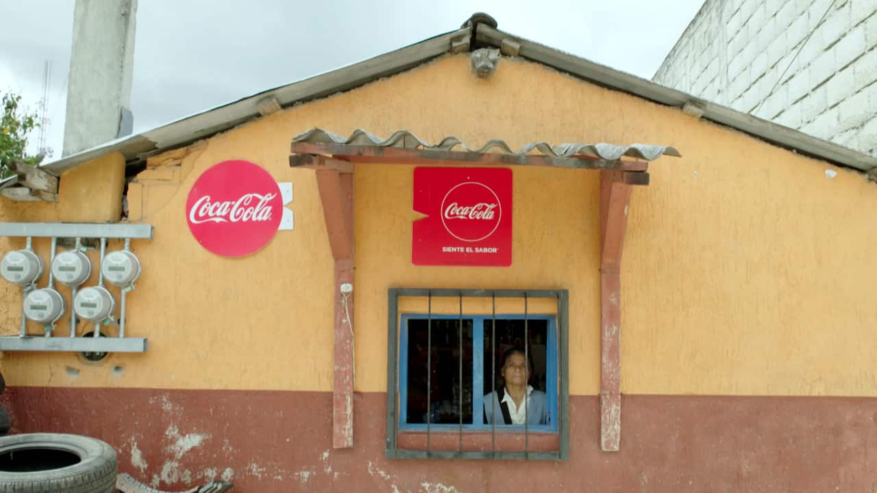 A woman looks out of a shop window with Coca-Cola advertisements on the walls.