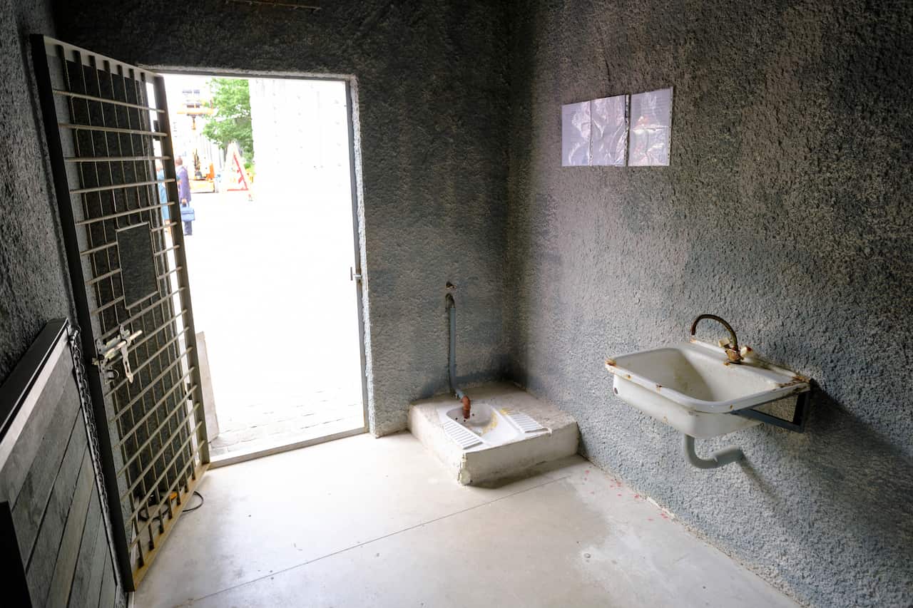 A reconstruction of a jail cell showing concrete walls, a barred door, a squat toilet, and a sink. 