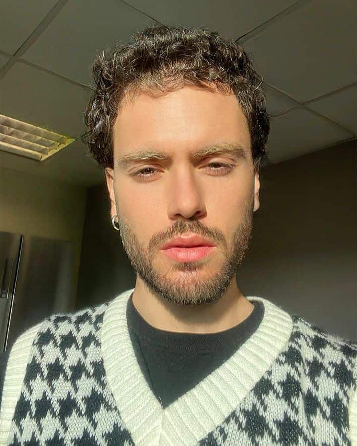 A young man in a houndstooth-patterned vest stares solemly into camera