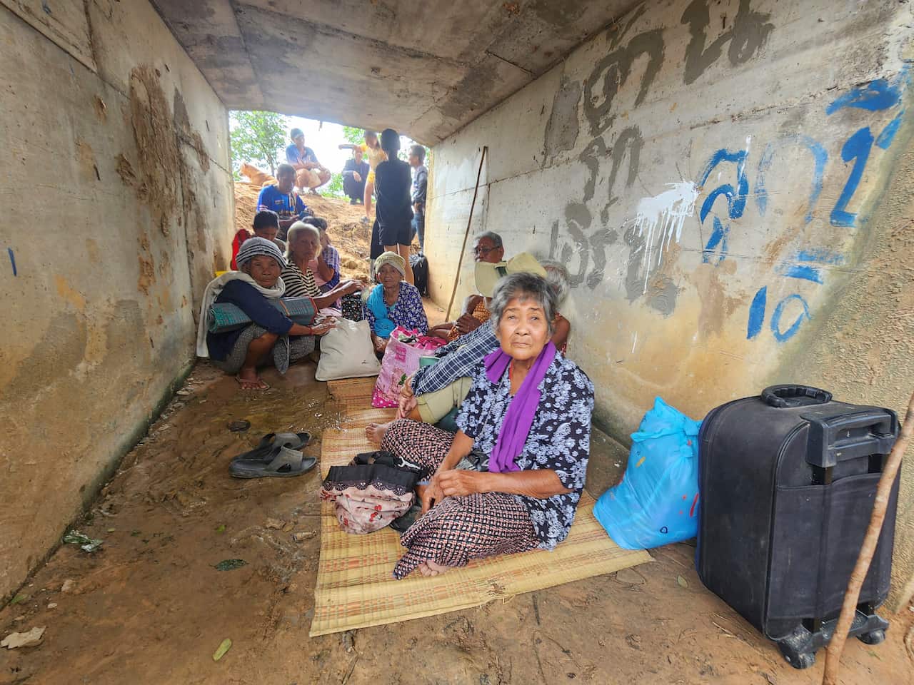 People sitting on the ground, inside a makeshift shelter.