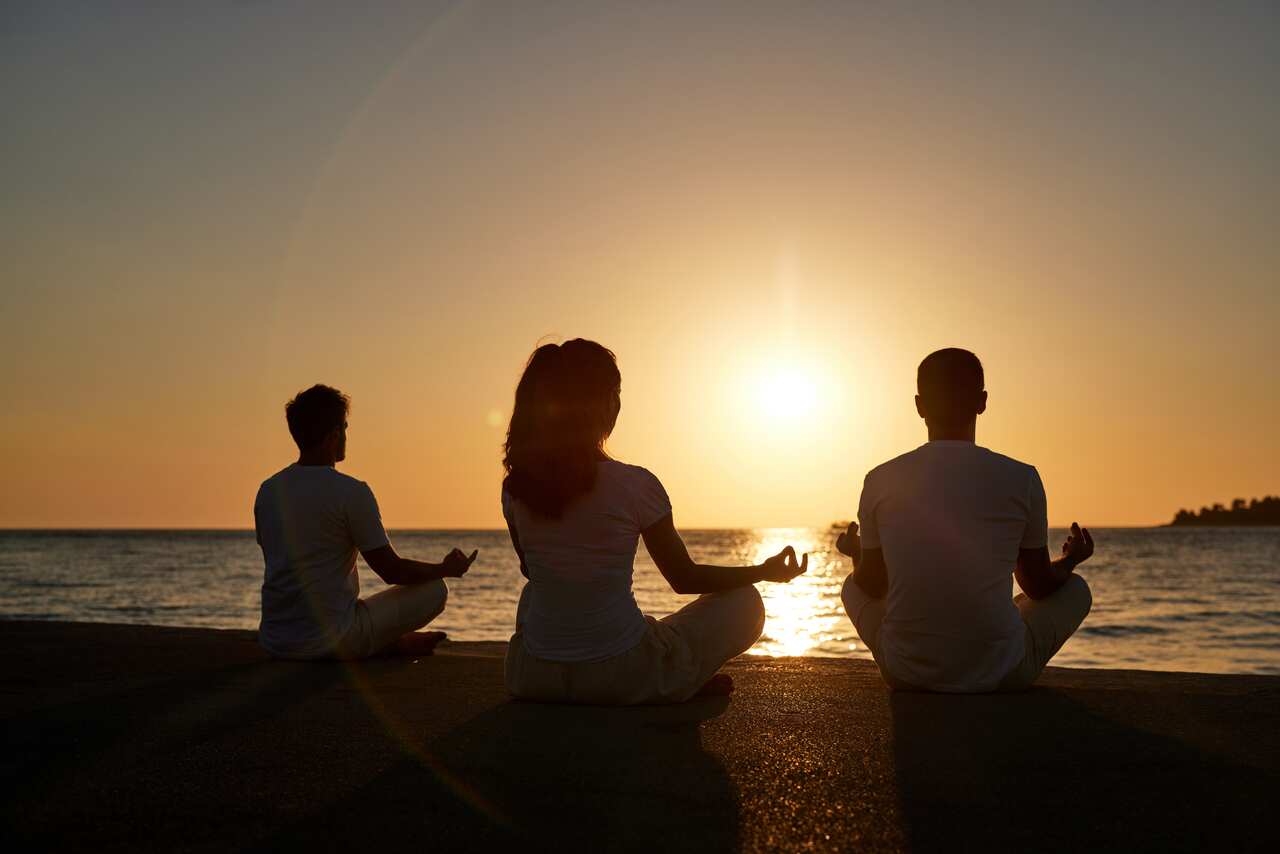 Back view of athletic people meditating on the beach at sunset.