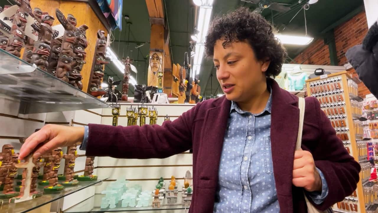 A woman with short curly hair and wearing a blue shirt with white dots and a burgundy coat is reaching out for a figurine at a souvenir shop