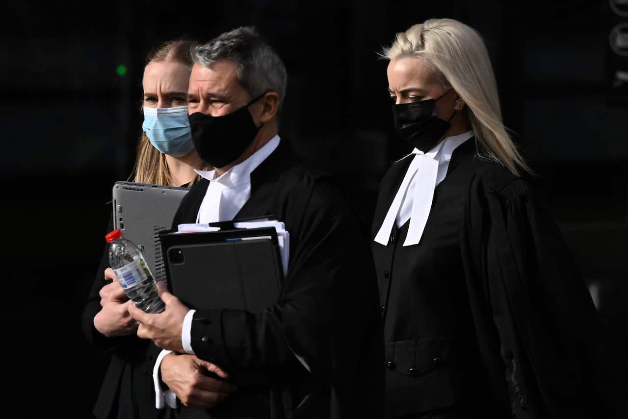 Two women and a man dressed in legal attire and masks are walking out, with furrowed eyebrows and serious facial expressions.