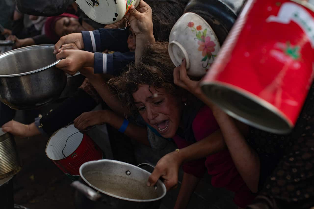 A group of tightly packed people hold pots in their hands for food