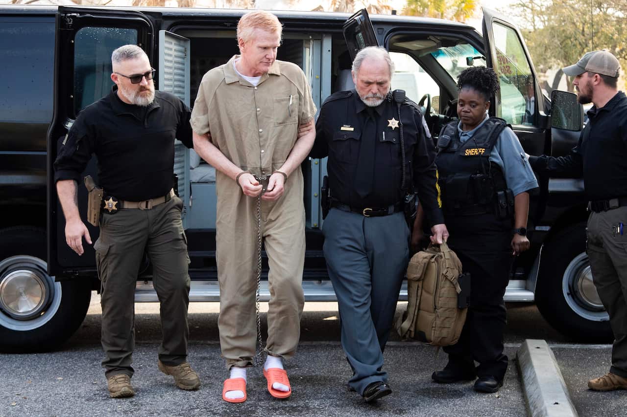 A man in handcuffs is escorted from a van by prison guards.