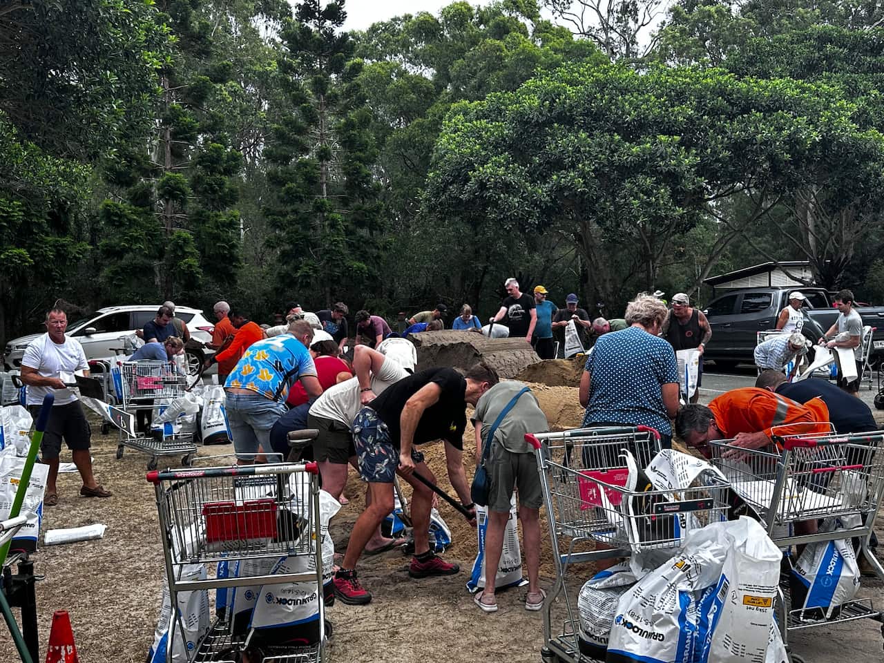 People with shovels around a pile of sand. There are shopping trolleys in the foreground 