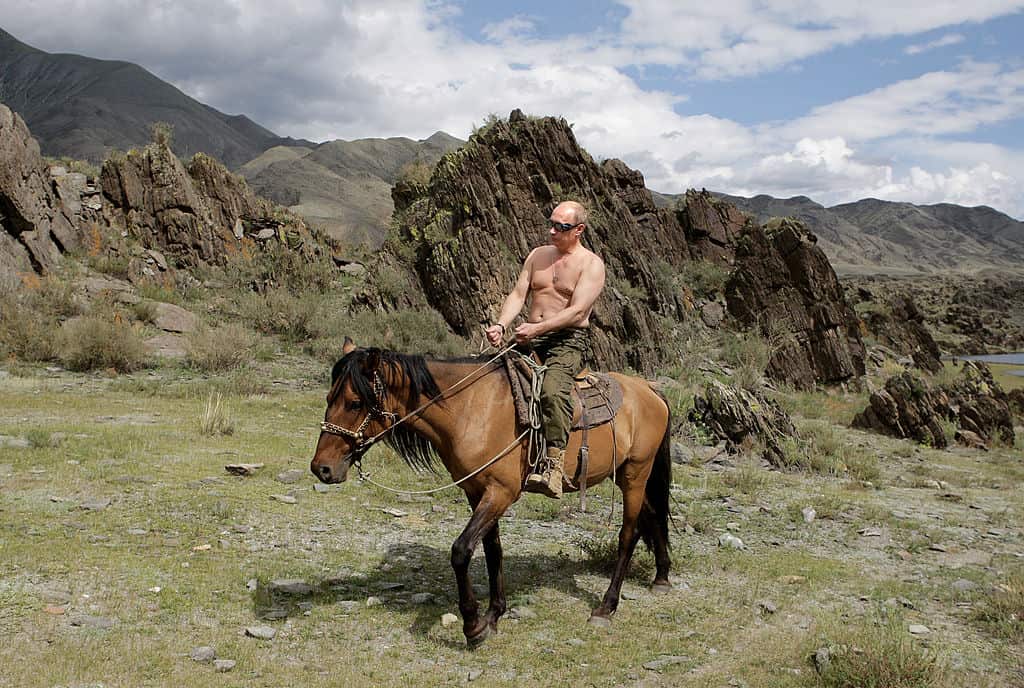 A bare-chested Vladimir Putin riding a horse in the mountains