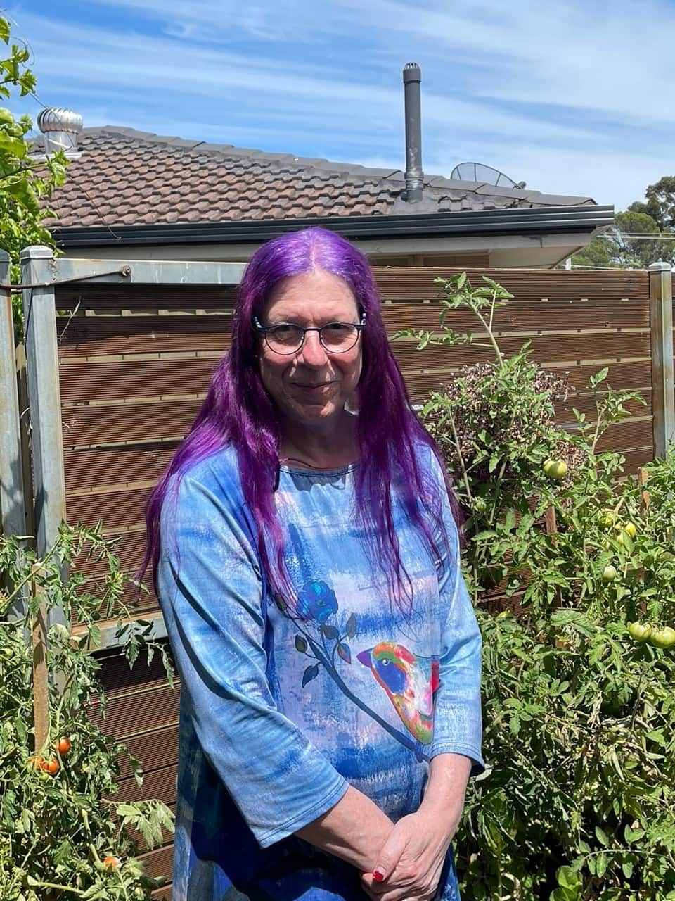 A woman with purple hair wearing a blue long-sleeved t-shirt and standing outside