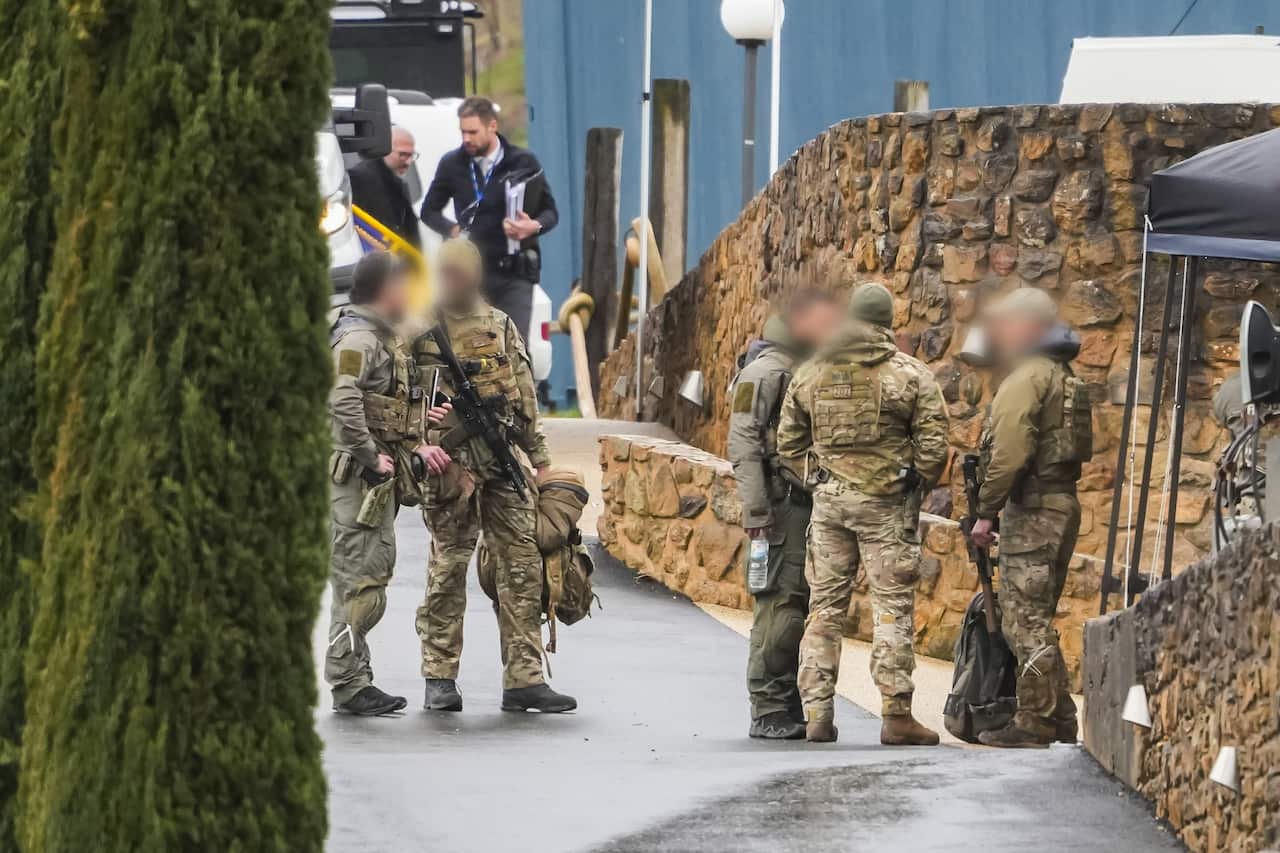 A group of men stand in army uniforms outside a building talking