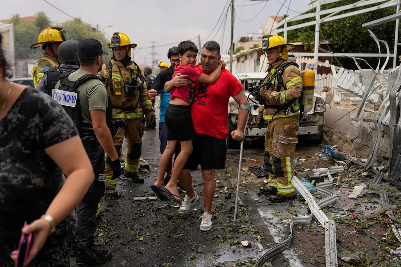 A man holds a child with building rubble around him