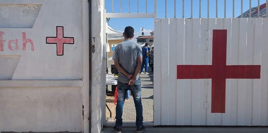 A man with his back turned and hands folded behind him stands at an entrance to a Red Cross field hospital.