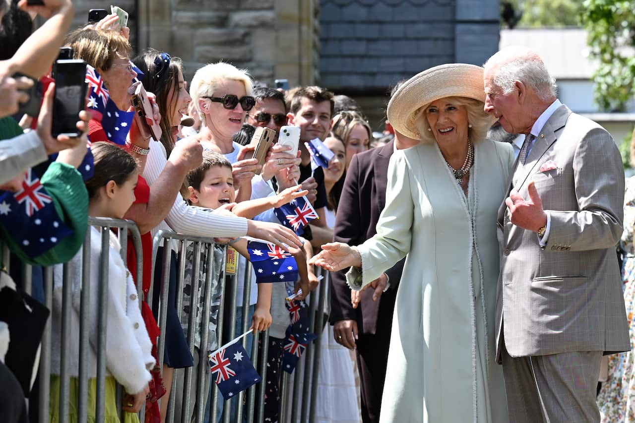 A woman in a hat and a man in a suit are greeted by their supporters who are behind a fence.
