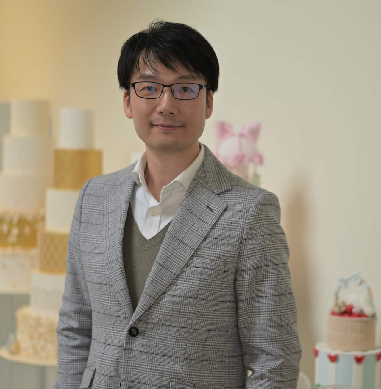 A man in a suit jacket stands in a cake shop looking at camera.