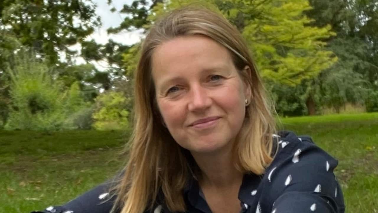 a close up on a middle aged woman with shoulder length blonde hair sitting on grass
