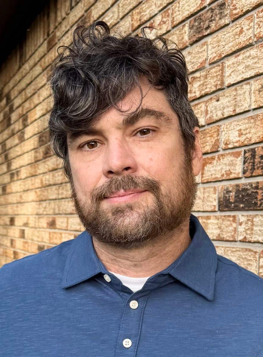 A close up of a man, who is wearing a blue shirt, posing for a photo.