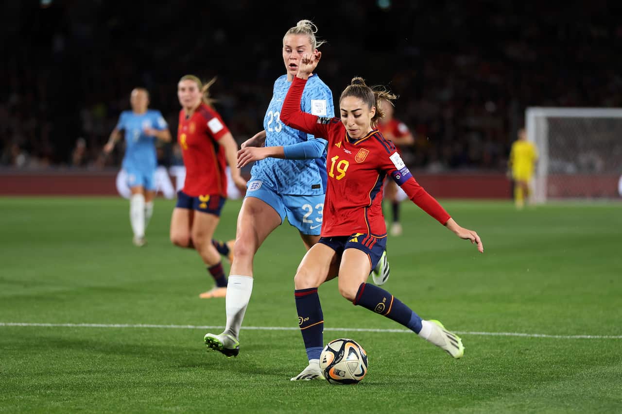 A woman in a red football jersey kicking the ball.