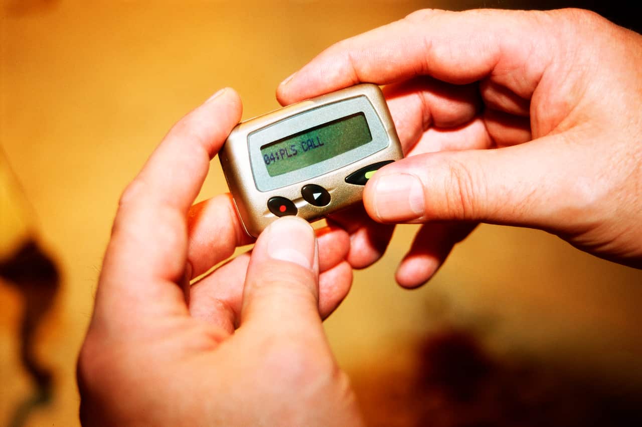 Hand holding a silver pager with a message on its screen
