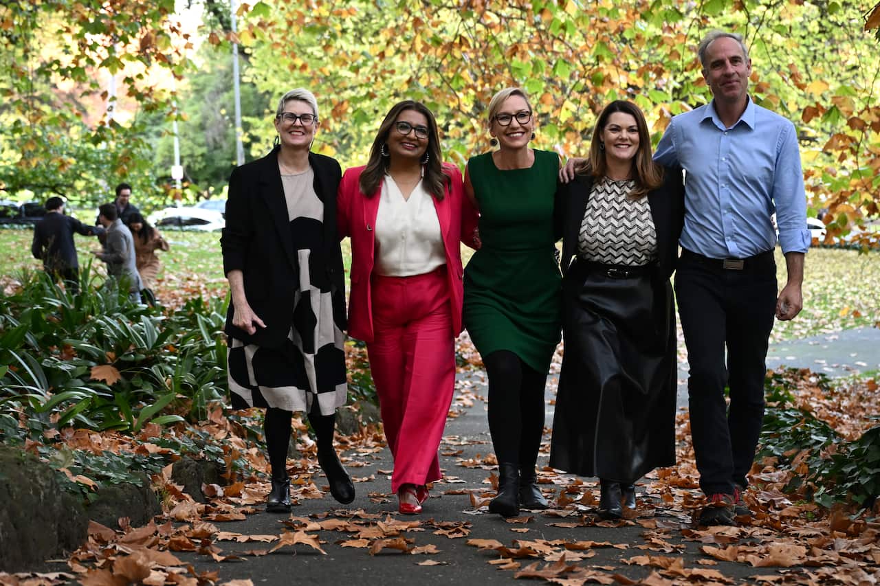 Five people smiling as they pose for a photo while standing outside.