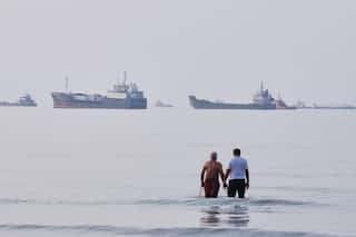 Two men wade in the waters of the Strait of Hormuz with vessels anchored in the background, off Bandar Abbas, Iran