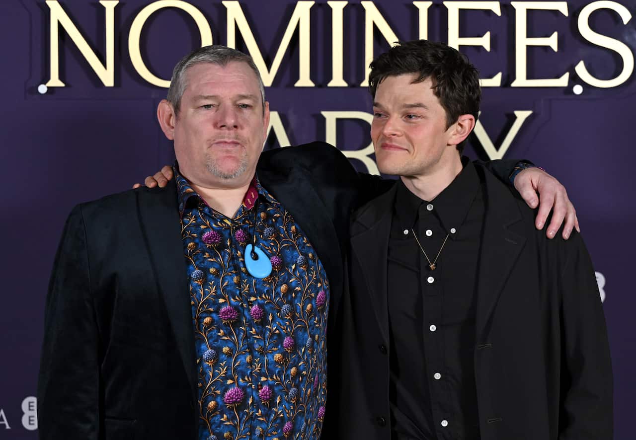 Two men embrace in front of a media wall for the cameras.