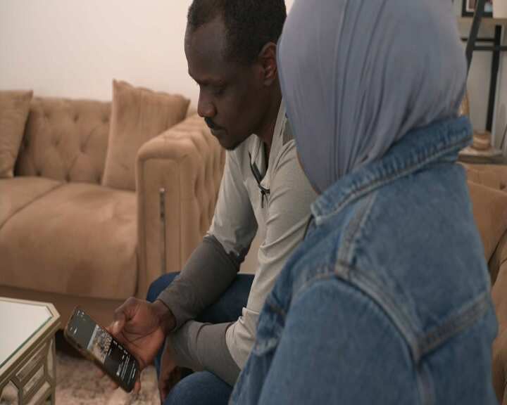 Man looking at his phone, sitting beside a woman wearing a blue hijab.