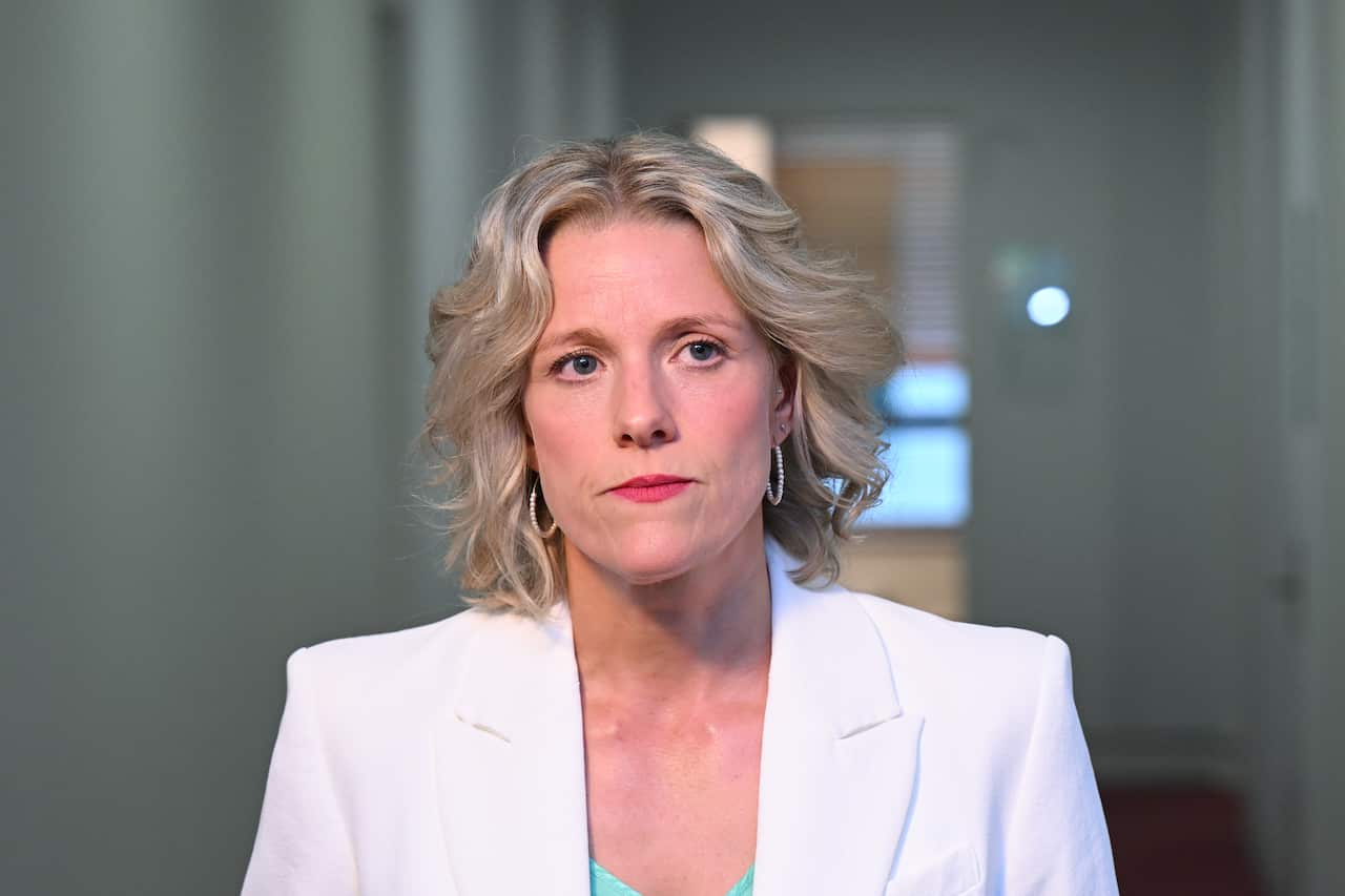 Clare O'Neil standing in a hallway, wearing a white blazer.