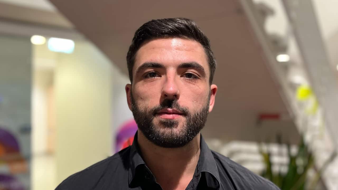 a closeup of a young man with brown hair and beard in an office