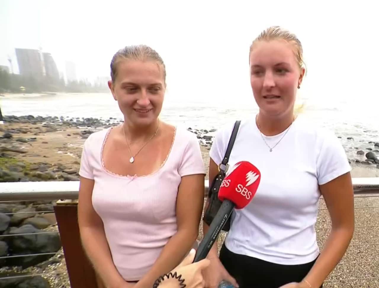 Two woman standing on a boardwalk near a beach. One is speaking to a journalist.