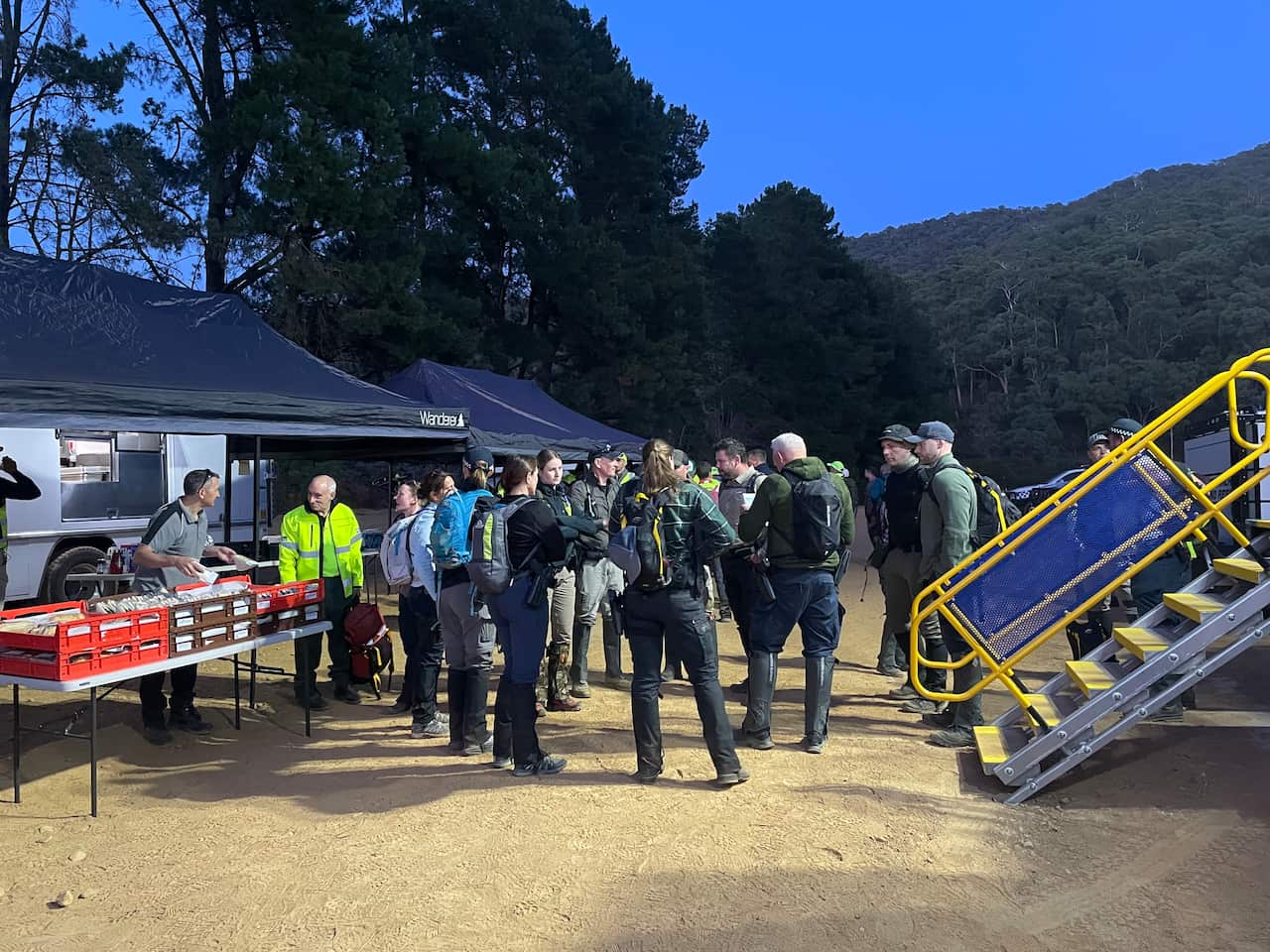 A group of people standing on a dirt path in front of bushland.