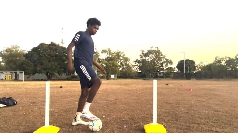A teenage boy in a black football kid has a football under his foot