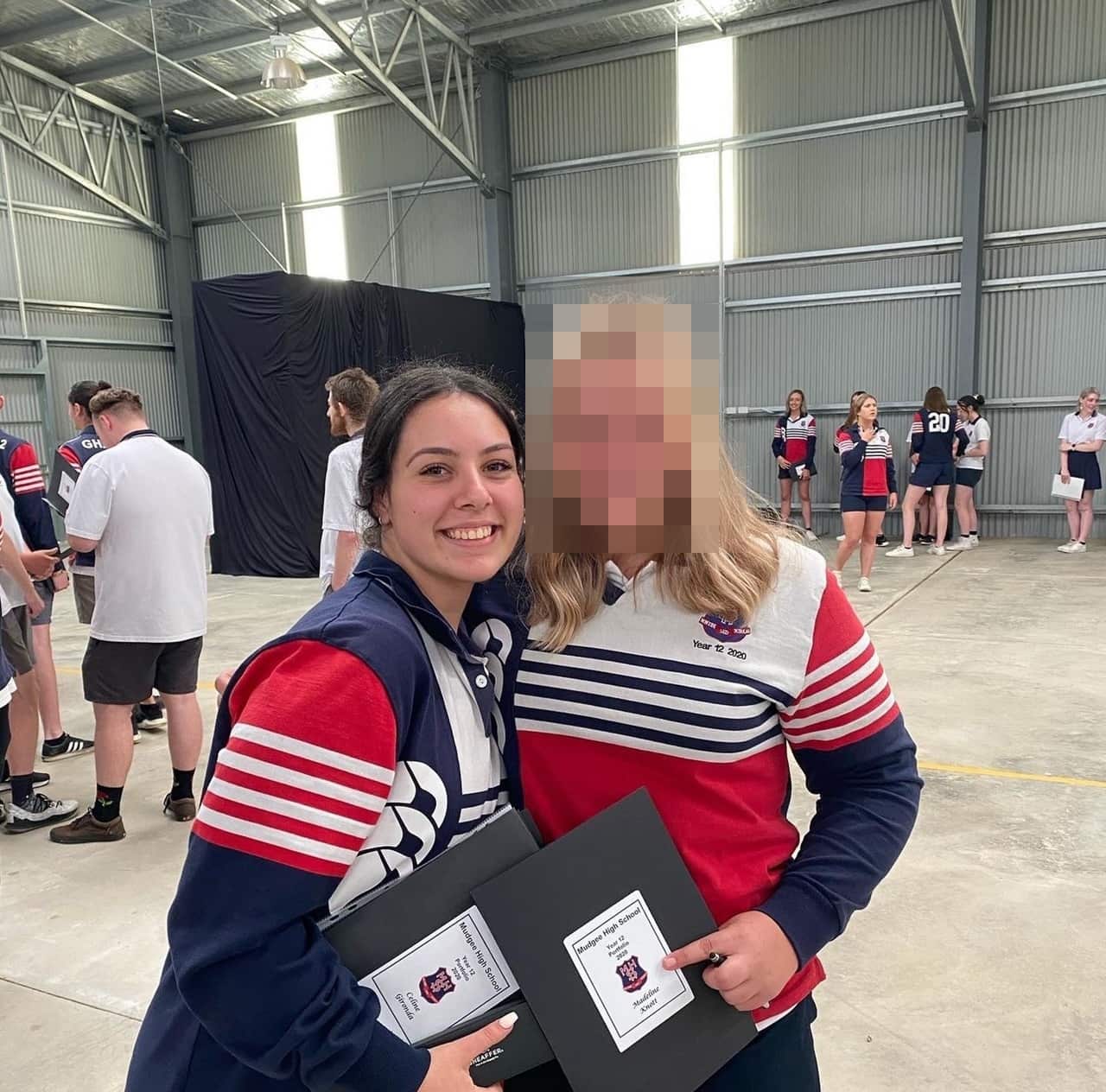 Two Y12 students in a school hall, celebrating graduating from high school as they embrace and smile at the camera.