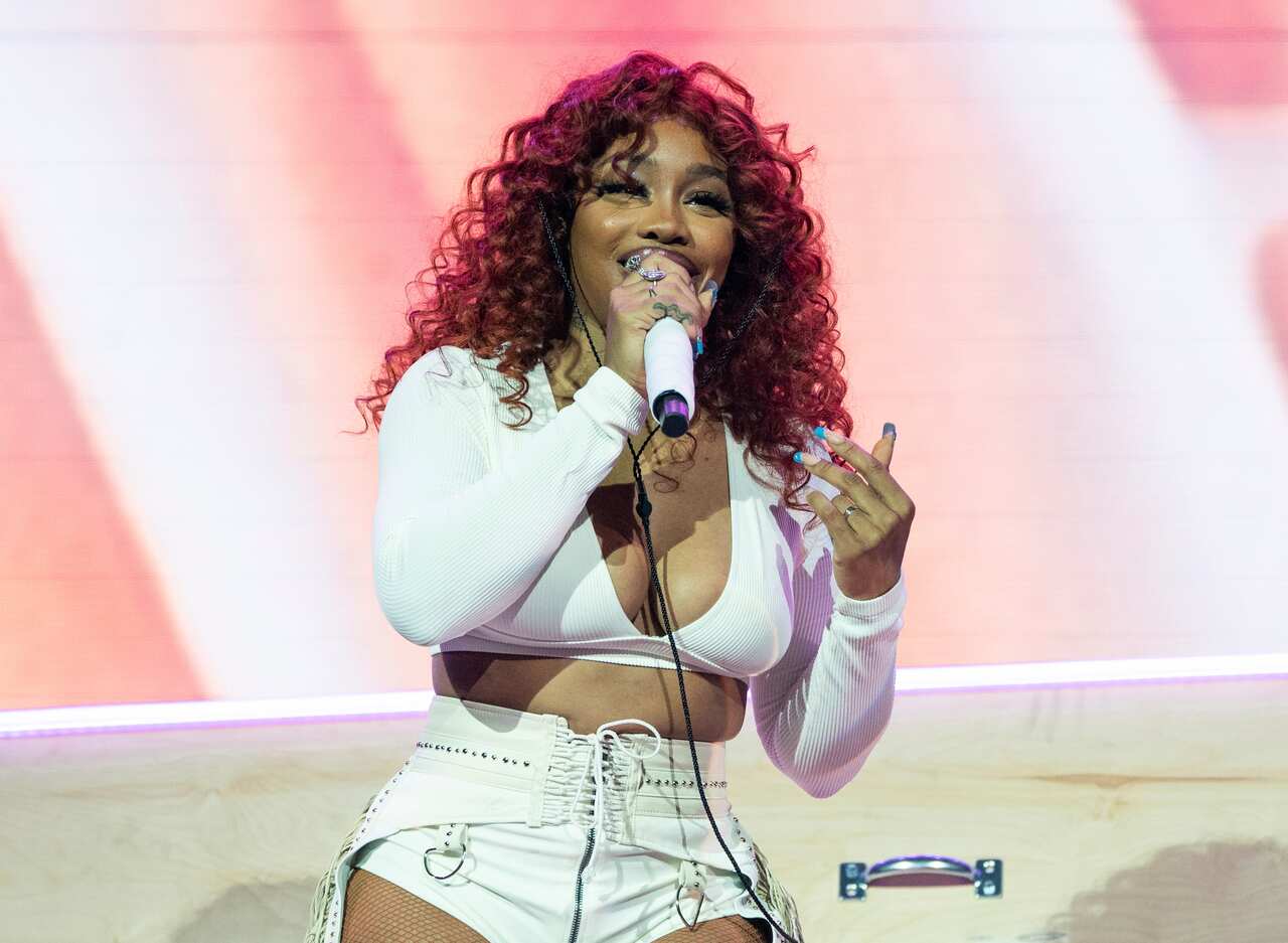 A woman wearing a white top and white shorts singing into a microphone she is holding.