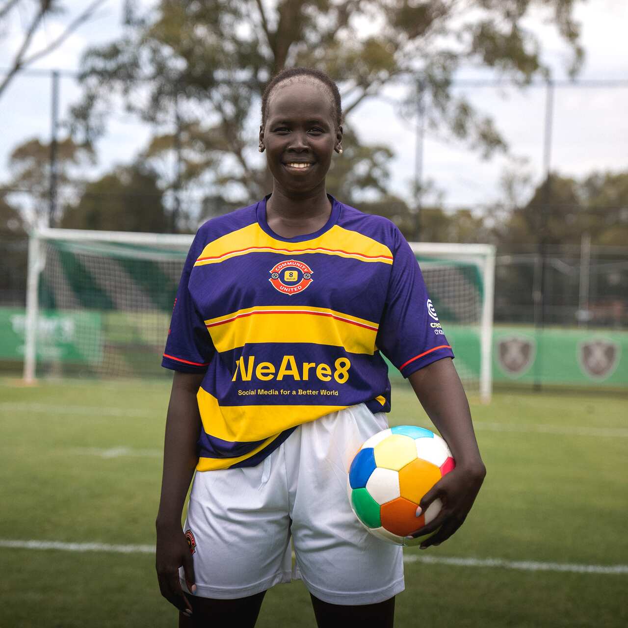 Anyier Yuol in her football kit, holding a football on a football pitch in front of a football goal.