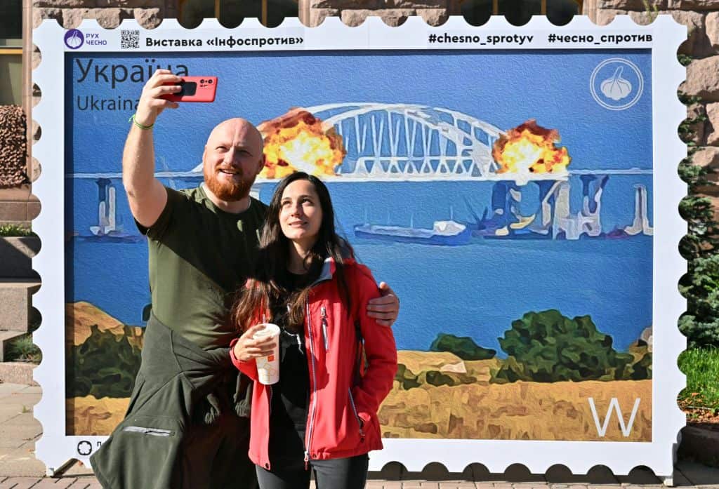 A couple takes a selfie in front of an artwork shaped as a big stamp entitled "Cotton to the Crimean Bridge" created by Andrusiv V, Serdyukov O, Kalinovska Y, Visich M depicting the bridge blast linking Russia and Crimea.
