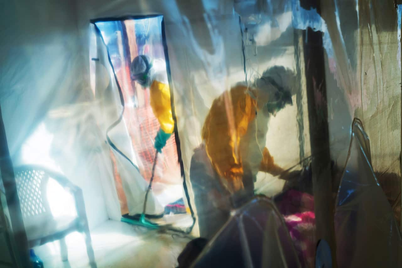 Health workers wearing protective suits tend to to a patient kept in an isolation tent.