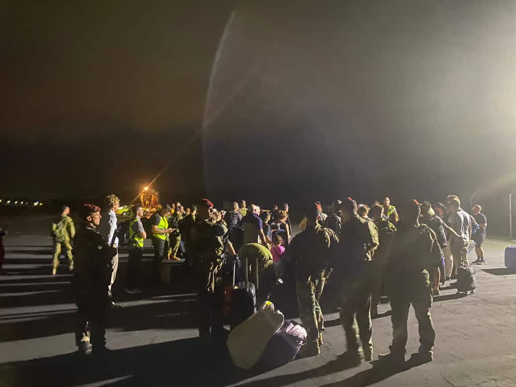 A group of people wait on the tarmac with luggage