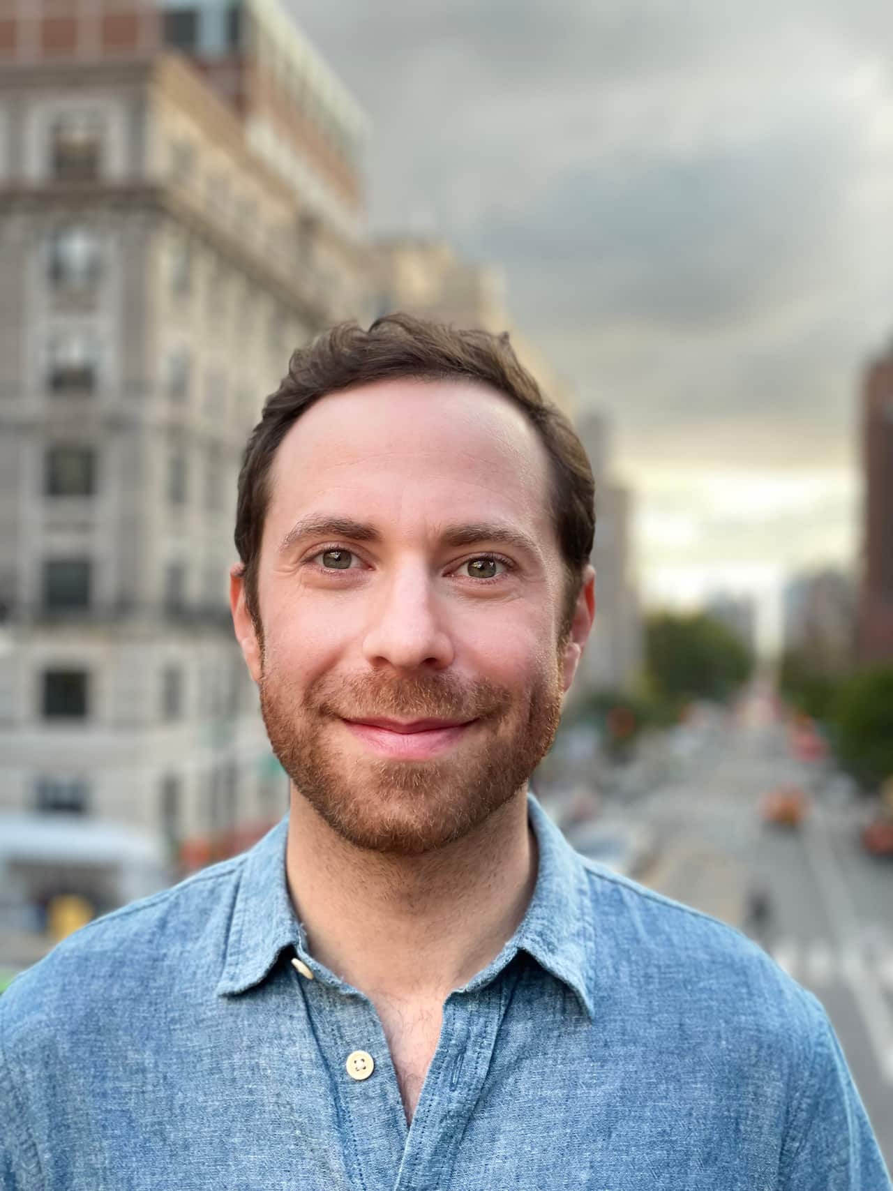A portrait shot of a man in a blue shirt smiling at the camera.