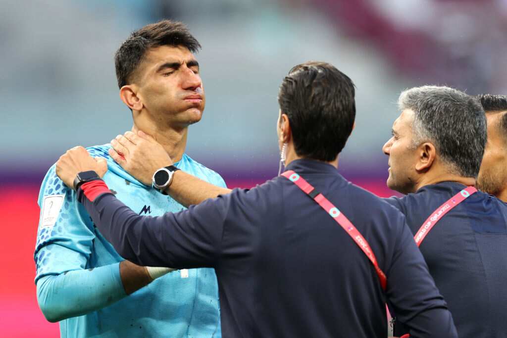 Two men show concern for the health of a goalkeeper, who is standing up