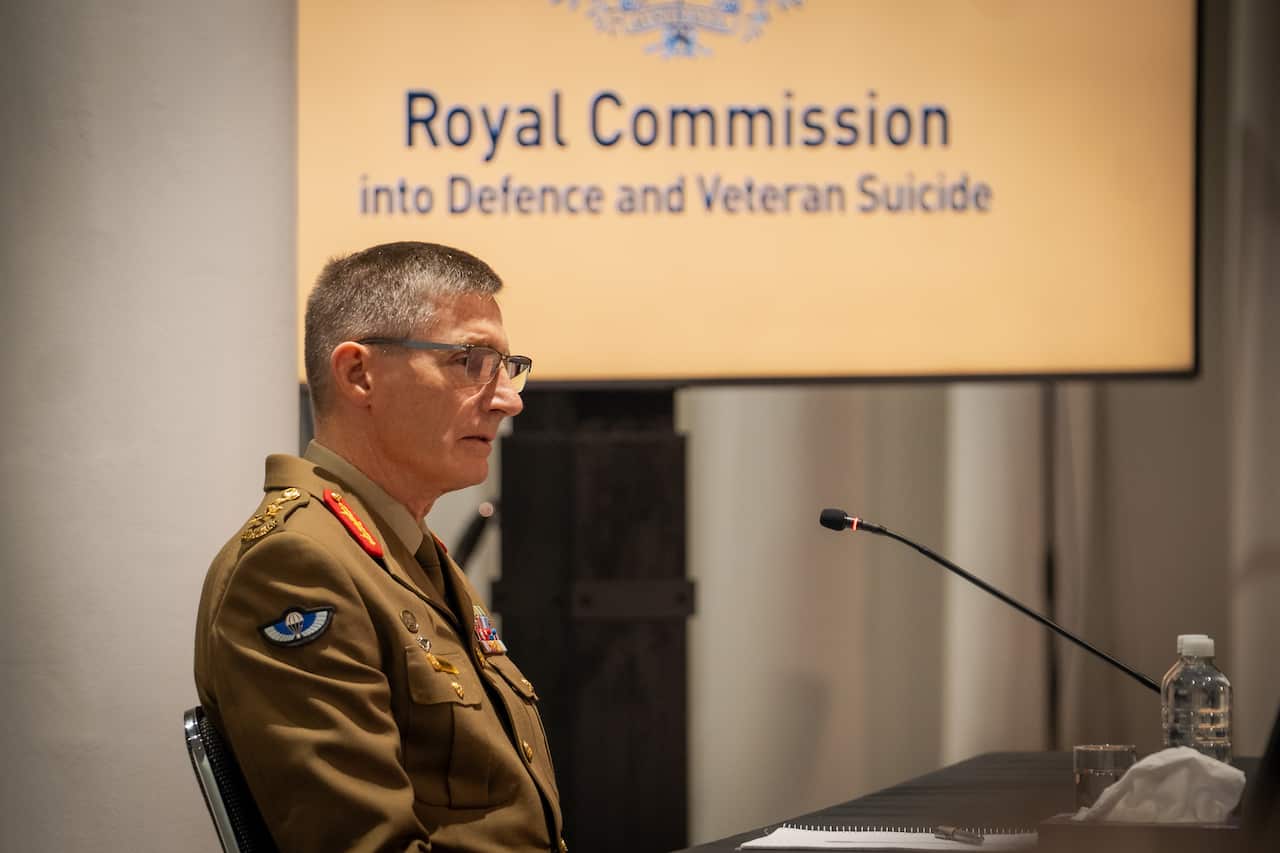 A man in a khaki military jacketspeaks in front of a microphone
