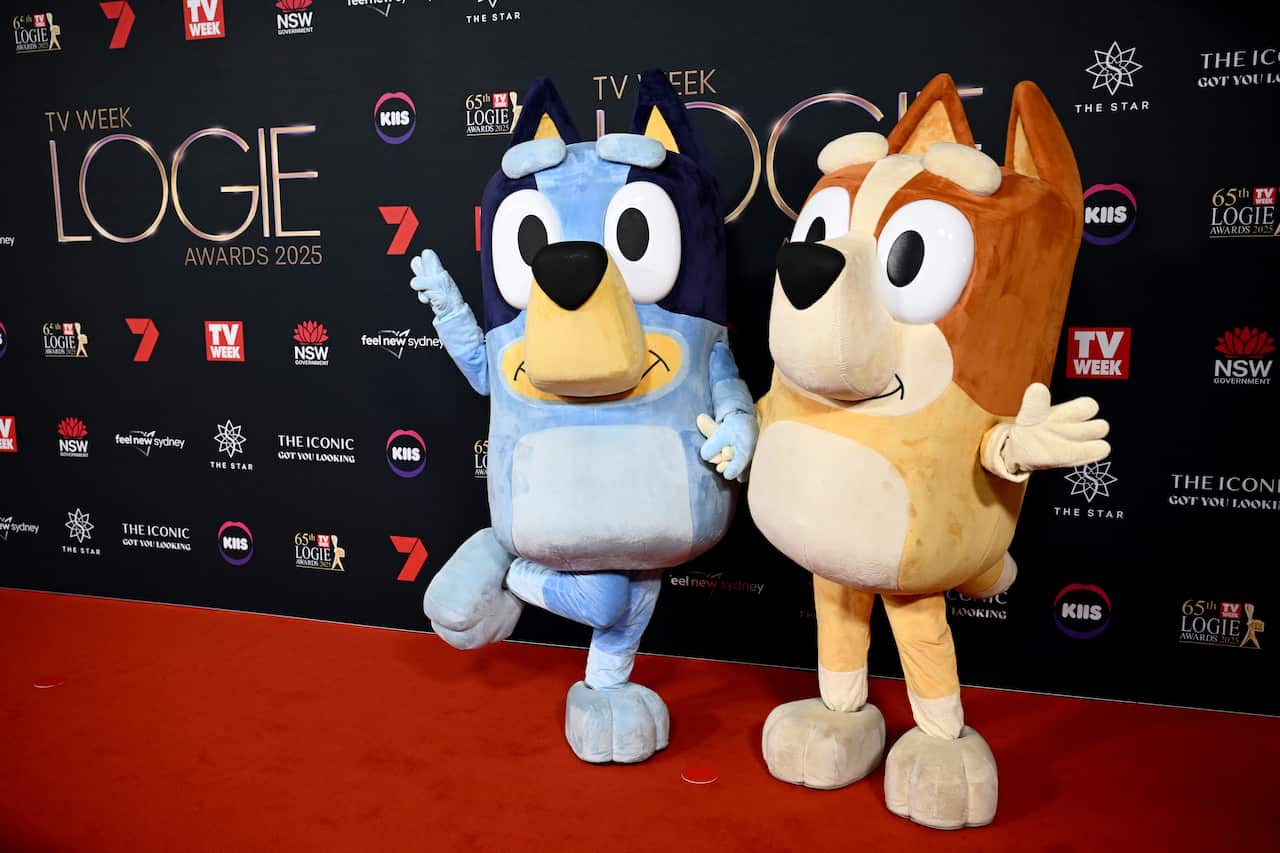 Two mascots wearing Bluey costumes on a red carpet.