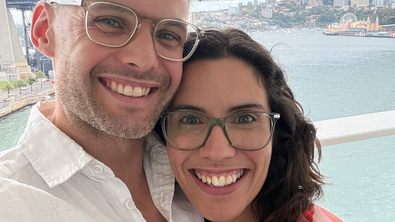 a man and woman both wearing glasses smiling in front of the sydney harbour